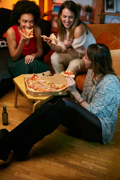 Felici amiche multiculturali che fanno festa a casa e mangiano pizza. - foto stock