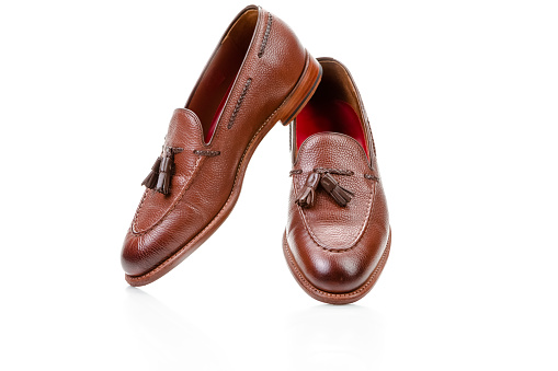 Footwear Ideas. Pair of Traditional Formal Stylish Brown Pebble Grain Tassel Loafer Shoes On White Surface. Horizontal image Composition