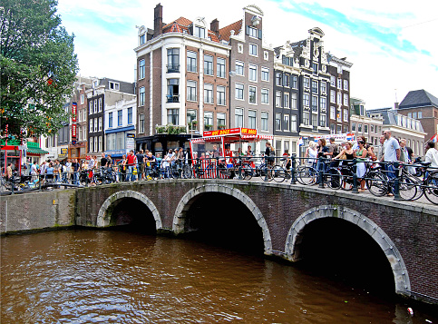 Bridges, canals, people and bicycles, distinctive Amsterdam, capital city, Netherlands, Amsterdam is renowned for its canal system, colourful narrow gabled facade terraced houses, liberal attitude towards the sex trade  and numerous bicycles, the principal form of transport in the city.