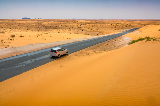 Car drives on a road in the Al Nefud Desert, near Jubbah, Saudi Arabia on a sunny day.