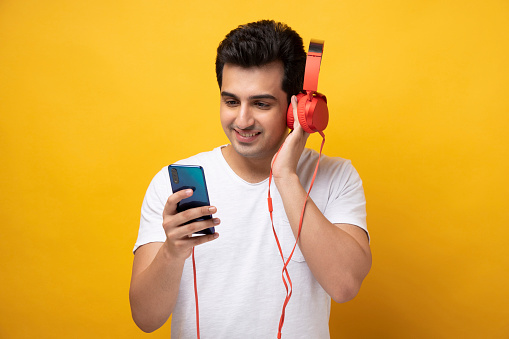 Cheerful young man in headphones using smartphone and listening to music while listening to music against red background