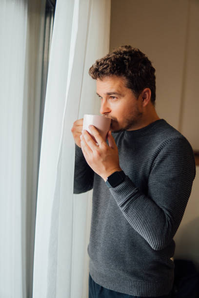 istock Man holding mug in his hand looking out the window 1359002886