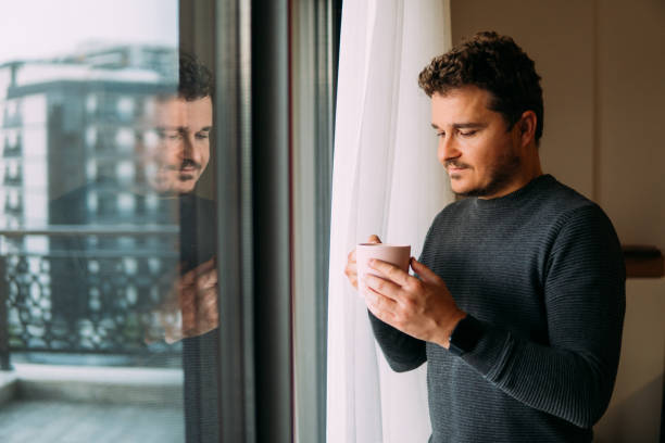 istock Man holding mug in his hand looking out the window 1359002918