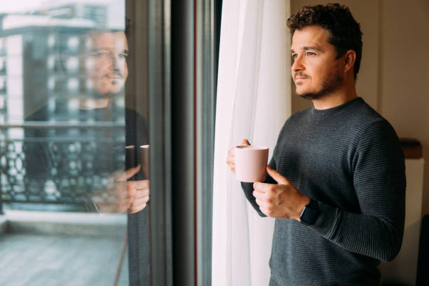 istock Man holding mug in his hand looking out the window 1359003018
