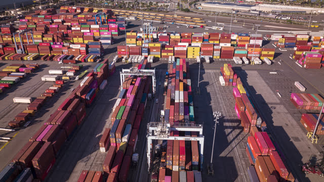 Aerial time lapse looking over a busy container terminal in the Port of Long Beach. Straddle carriers and top handlers are taking shipping containers off trucks and stacking them in rows, while a freight train passes by in the distance. 

This shot was taken at the end of 2021 during the global supply chain crisis.