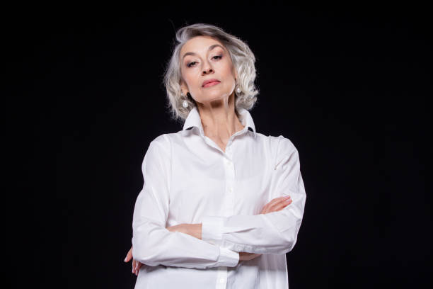 Portrait of a domineering, arrogant mature woman looking down and standing with her arms crossed isolated on a black background Portrait of a domineering, arrogant mature woman looking down and standing with her arms crossed isolated on a black background. arrogance stock pictures, royalty-free photos & images