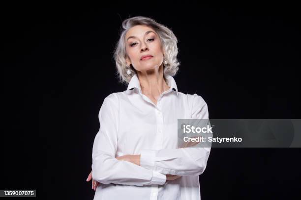 Portrait Of A Domineering Arrogant Mature Woman Looking Down And Standing With Her Arms Crossed Isolated On A Black Background Stock Photo - Download Image Now