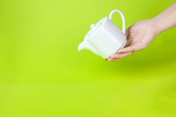 istock Cute White ceramic teapot against light green background. Contemporary style. 1359008970