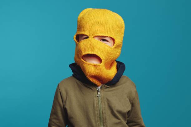 Cute kid wearing yellow knitted thief mask, isolated over blue