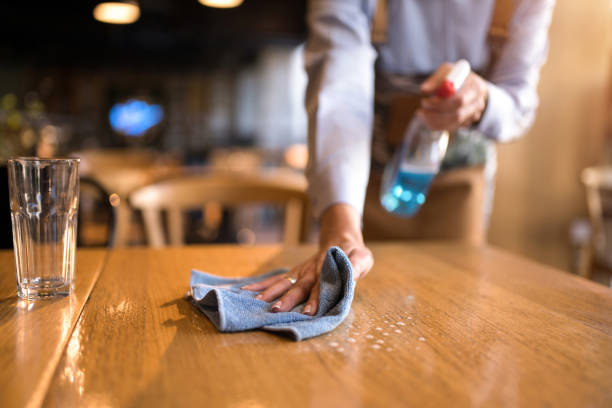 istock Waitress cleaning tables with disinfectant in a cafe. 1359011173