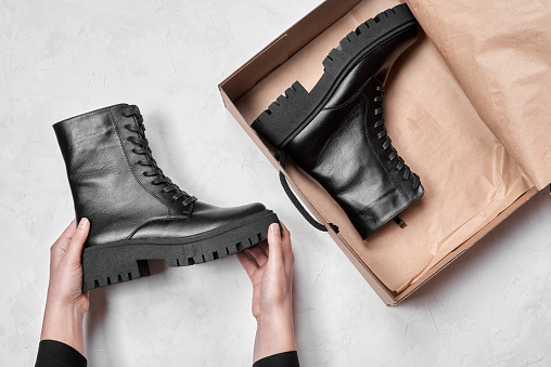 Woman holding in hands black leather female boots in box isolated on gray background, copy space. Top view, flat lay