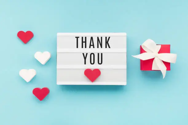 Photo of Thank You or thanks greeting card, white lightbox, hearts and red gift box on blue background, top view