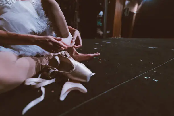 Photo of a ballerina checking and putting her ballet shoes on while getting ready for her performance.