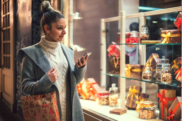 Teenage girl shopping Christmas gifts Teenage girl using cell phone while shopping Christmas gifts in the city. window shopping at night stock pictures, royalty-free photos & images