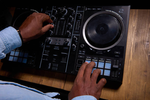 Black man DJ uses control desk to create song.