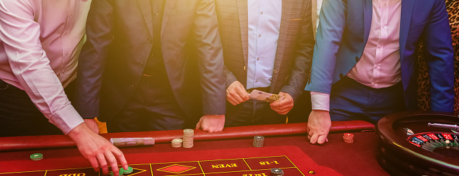 Group of people behind roulette gambling table in luxury casino. Friends playing poker at roulette table with tape measure. Vegas games nightlife lucky winning concept. Banner