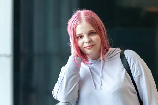 Close up outdoors portrait of attractive 20 year old woman with pink hair in purple hooded shirt
