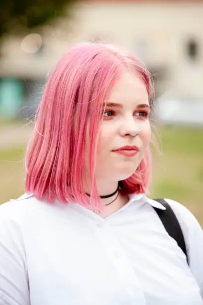 Close up outdoors portrait of attractive 20 year old woman with pink hair in white shirt