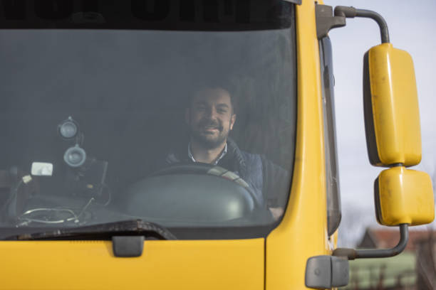 Truck driver sitting in cabin and smiling while looking in camera, view through windshield