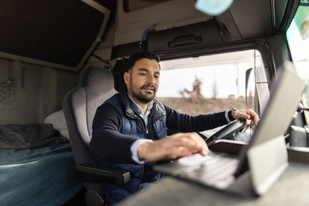 camionista che digita la destinazione su tablet mentre è seduto in cabina - trasporto merci via terra foto e immagini stock
