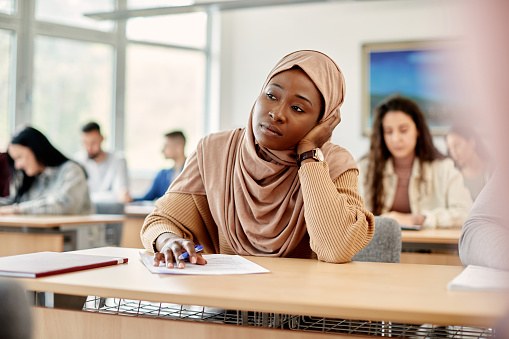 Pensive African student in hijab attending a class at university classroom.