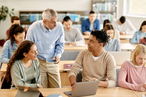 istock Mature teacher and his students talking while using laptop during lecture at the university. 1359027655