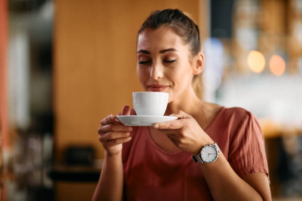 Young woman enjoying in smell of fresh coffee in a cafe. Smiling woman enjoying with eyes closed in cup of fresh coffee at cafe. coffee stock pictures, royalty-free photos & images