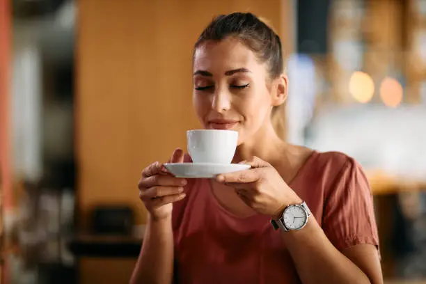 Smiling woman enjoying with eyes closed in cup of fresh coffee at cafe.
