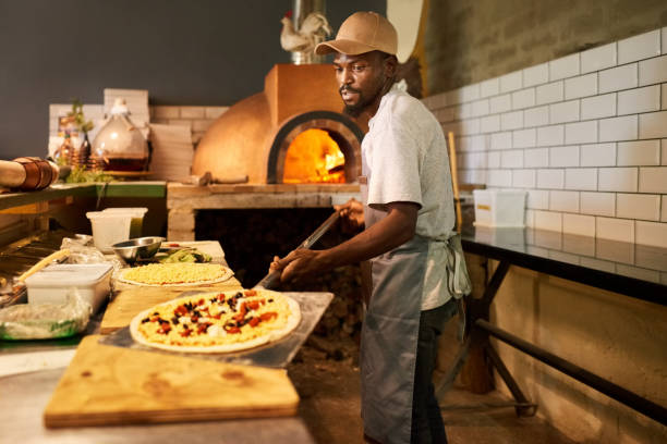 homme travaillant dans la cuisine d’un restaurant à préparer des pizzas traditionnelles - chef restaurant cooking african descent photos et images de collection