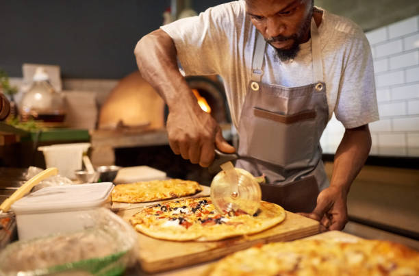 Chef preparing pizza at pizzeria Chef with a pizza cutter cutting pizza to pieces at pizzeria pizza cutter stock pictures, royalty-free photos & images
