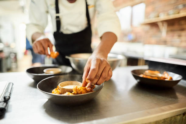 Restaurant chef preparing a dish Close-up of male chef arranging food on a dish in the commercial kitchen busy restaurant tables stock pictures, royalty-free photos & images