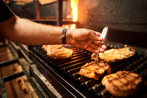 Close-up of a male chef hand checking core temperature of steak on grill using meat thermometer in restaurant kitchen