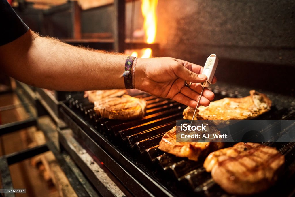 Measuring temperature of steak on grill Close-up of a male chef hand checking core temperature of steak on grill using meat thermometer in restaurant kitchen Thermometer Stock Photo