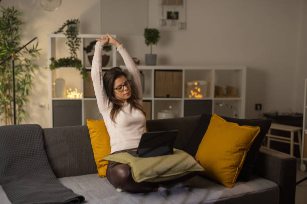 istock Beautiful woman sitting on sofa in living room and using tablet while stretching arms 1359030944