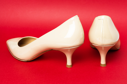 Classic beige patent leather shoes  with kitten heels on red background, back view.