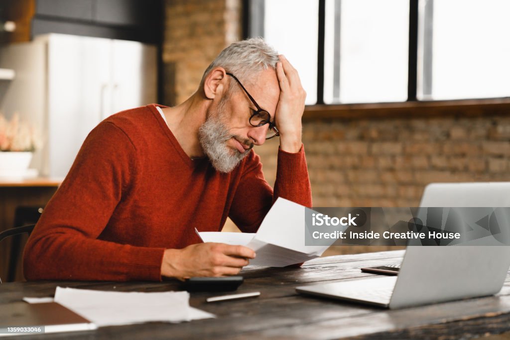 Expensive charges on domestic bills. Loan, debt, bunkruptcy concept. Sad depressed caucasian businessman holding documents, having problems with dismissal at home office Financial Bill Stock Photo