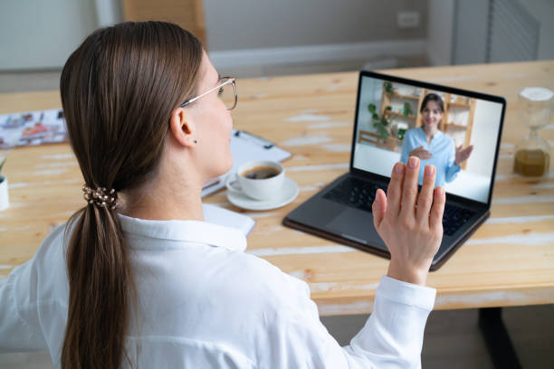 istock Woman sitting at desk, using computer and waving to webcam. 1359033231
