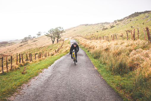 Young caucasian cyclist man sprinting while climbing a hill in a foggy mountain.