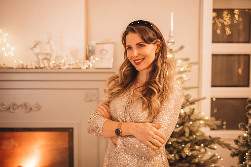 Christmas portrait. Woman wearing sparkly elegant dress. Evening or night with fireplace in background.