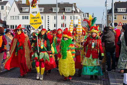 Maastricht, Limburg, Netherlands, february 10th 2013, a group of cheerful men and women wearing yellow/red/green ceremonial make-up and costumes walking along in the sunday carnaval parade on the famous 13th century 'Sint Servaasbrug' over the Meuse river in Maastricht (the oldest bridge in the Netherlands) - people are standing side by side on both sides of the road to watch the parade - with over 3 million annual visitors the city is a popular travel destination