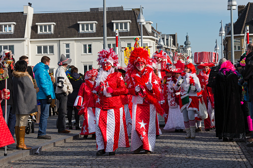 Maastricht, Limburg, Netherlands, february 10th 2013, a group of cheerful women wearing white/red ceremonial make-up and costumes with feathers, walking along in the sunday carnaval parade on the famous 13th century 'Sint Servaasbrug' over the Meuse river in Maastricht (the oldest bridge in the Netherlands) - people are standing side by side on both sides of the road to watch the parade - with over 3 million annual visitors the city is a popular travel destination
