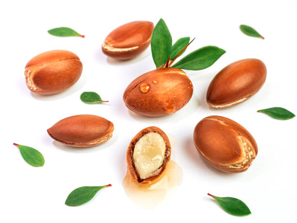 istock Argan nuts with green leaves on an isolated white background. Chopped argan nut with a drop of oil. Whole and half Moroccan Argania Spinosa seeds for the production of oil 1359042292