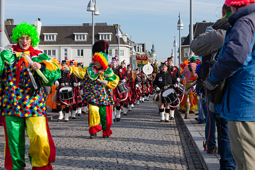Maastricht, Limburg, Netherlands, february 10th 2013, a marching band wearing costumes with kilts walking along in the sunday carnaval parade on the famous 13th century 'Sint Servaasbrug' over the Meuse river in Maastricht (the oldest bridge in the Netherlands) - they are preceded by some cheerful clowns while people are standing side by side on both sides of the road to watch the parade - with over 3 million annual visitors the city is a popular travel destination