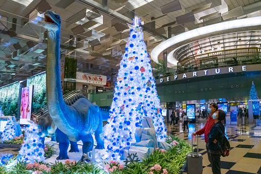Singapore, Singapore - December 12, 2021: A couple look at dinosaur-themed Christmas decorations outside the departure area of Terminal 3, Changi Airport.
