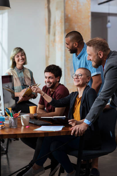 The best office team in town Smiling young colleagues working in an office space while looking at a desktop computer workplace diversity vertical stock pictures, royalty-free photos & images