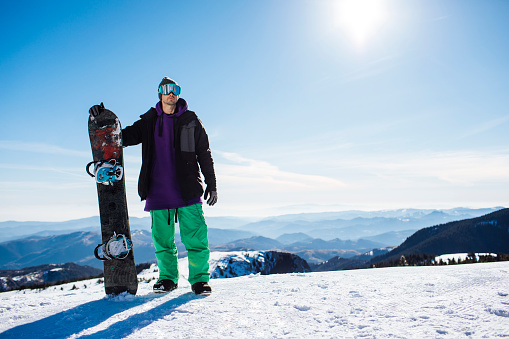 Portrait shot of a young man in the mountains, holding his snowboard, ready for winter sports