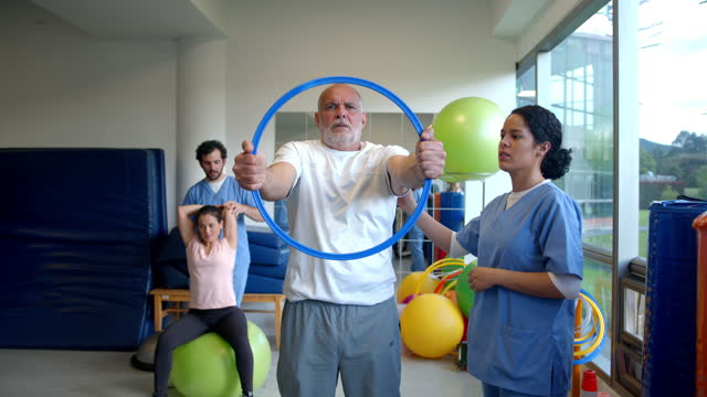 Senior male patient working out his shoulders and arms with a hoop following his therapist instructions
