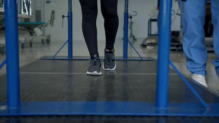 Unrecognizable patient walking with the help of parallel bars while therapist walks beside her