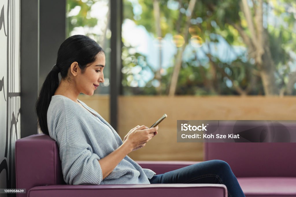 Side profile of an Indian woman looking down at her phone while smiling Women Stock Photo