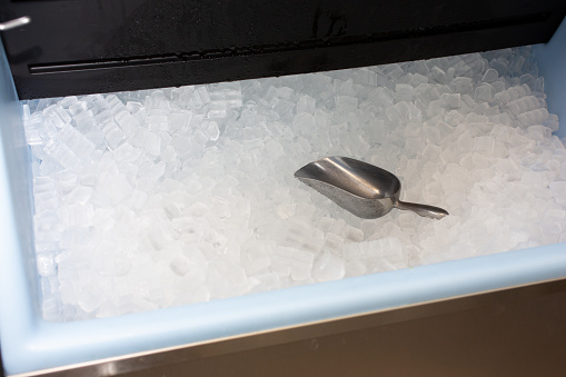 A view of a metal scooper inside a fully stocked ice machine.